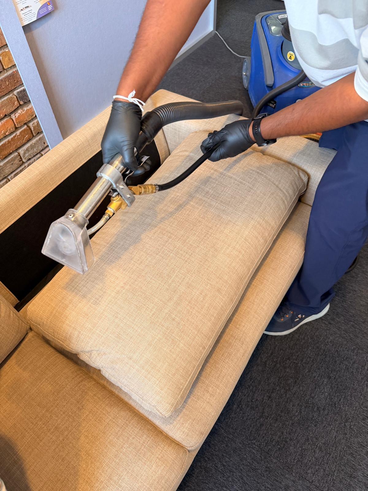 Gloved hands steam cleaning a beige fabric couch cushion