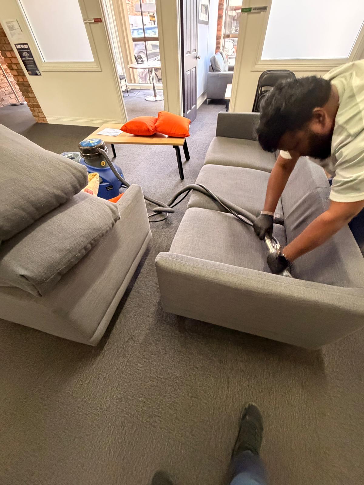 Cleaner steam cleaning a grey fabric sofa in a reception lounge